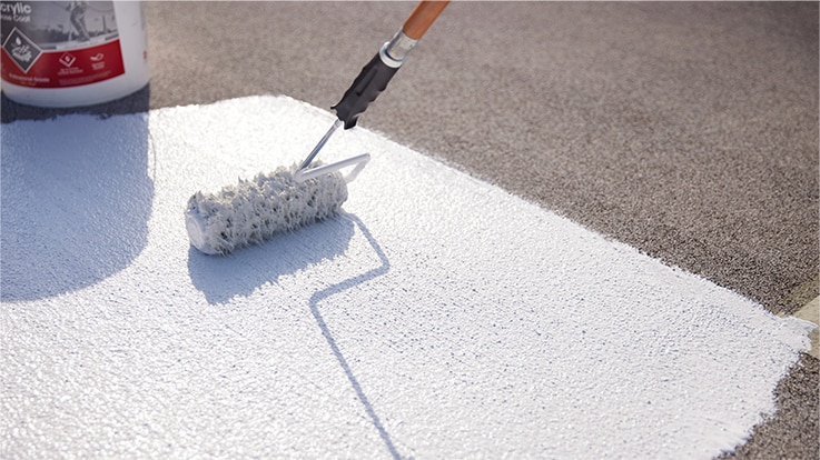 A paint roller applies white coating to an asphalt surface under bright sunlight.